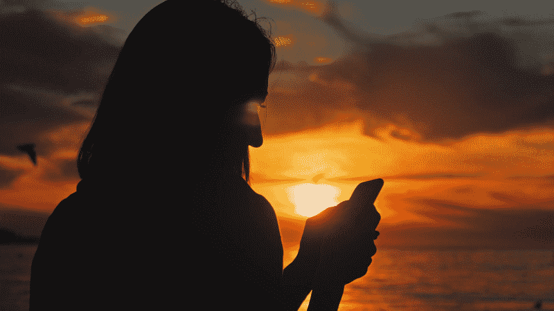 Person using cell phone at sunset
